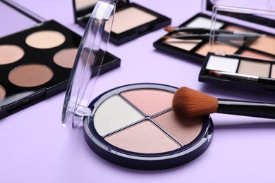 Photo of Colorful contouring palettes with brushes on violet background, closeup. Professional cosmetic product