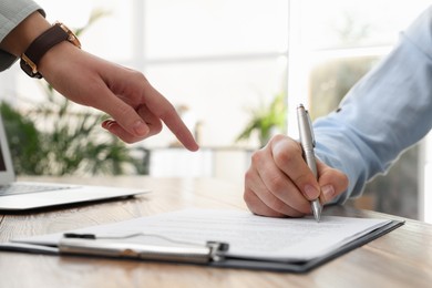 Businesspeople signing contract at table in office, closeup