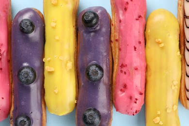 Photo of Delicious eclairs covered with glaze on light blue background, top view