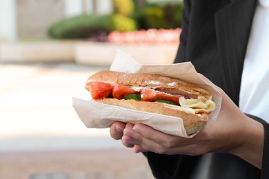 Photo of Woman holding tasty sandwich with vegetables outdoors, closeup and space for text. Street food