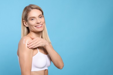 Photo of Woman applying body cream onto her arm against light blue background, space for text