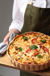 Photo of Woman holding board with tasty quiche on grey background, closeup