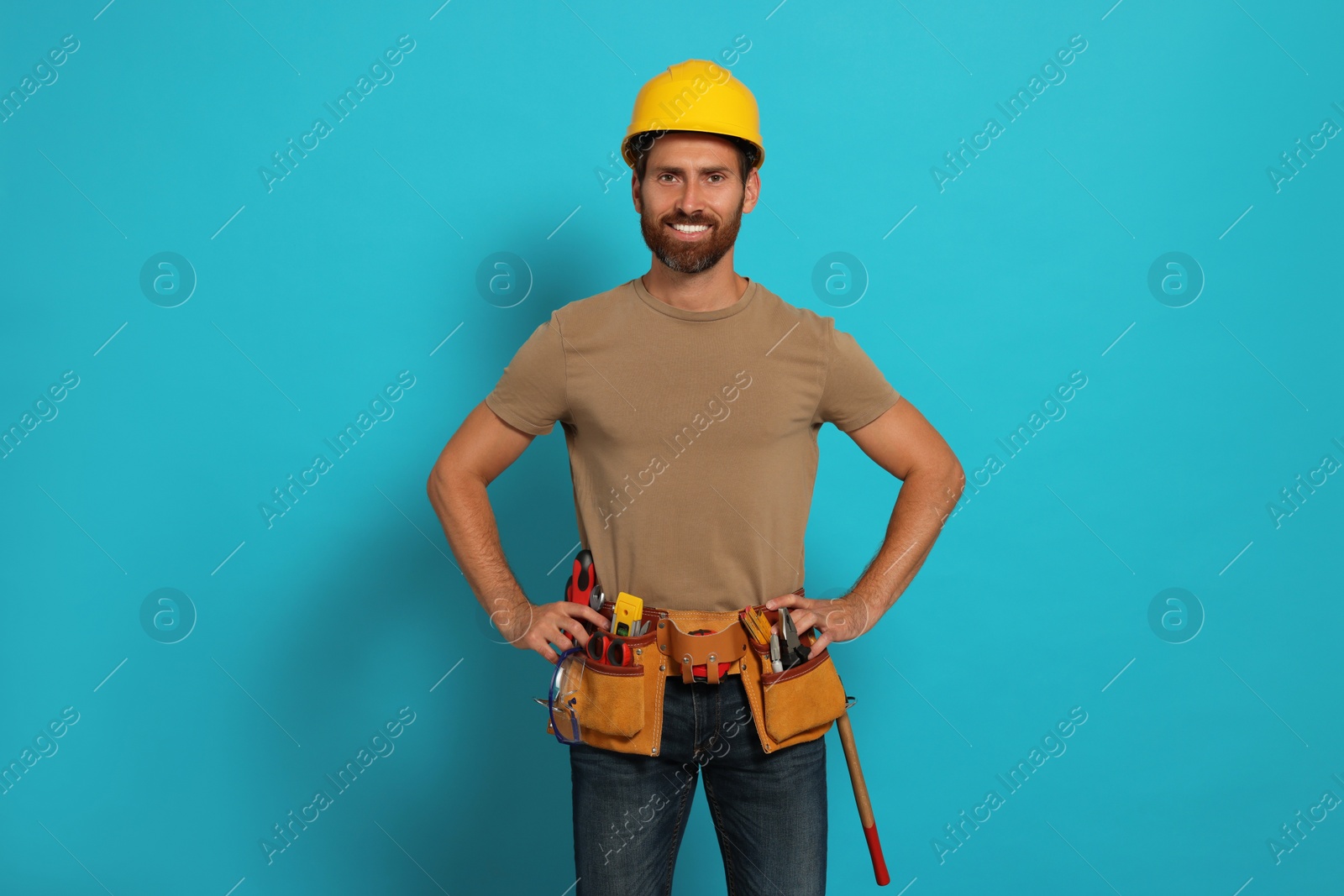 Photo of Professional builder in hard hat with tool belt on light blue background