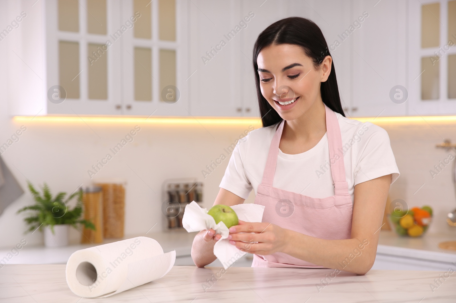 Photo of Woman wiping green apple with paper towel in kitchen