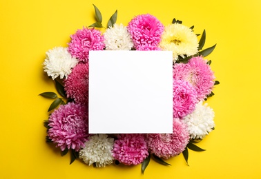 Photo of Flat lay composition with blank card and beautiful asters on yellow background, space for text. Autumn flowers