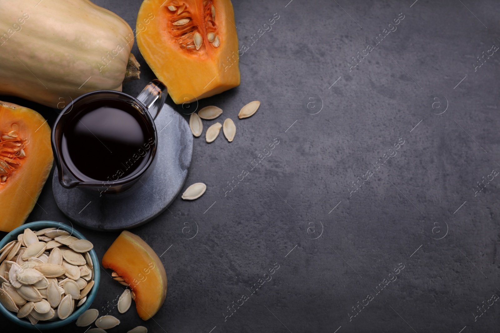 Photo of Fresh pumpkin seed oil in glass pitcher on dark grey table, flat lay. Space for text