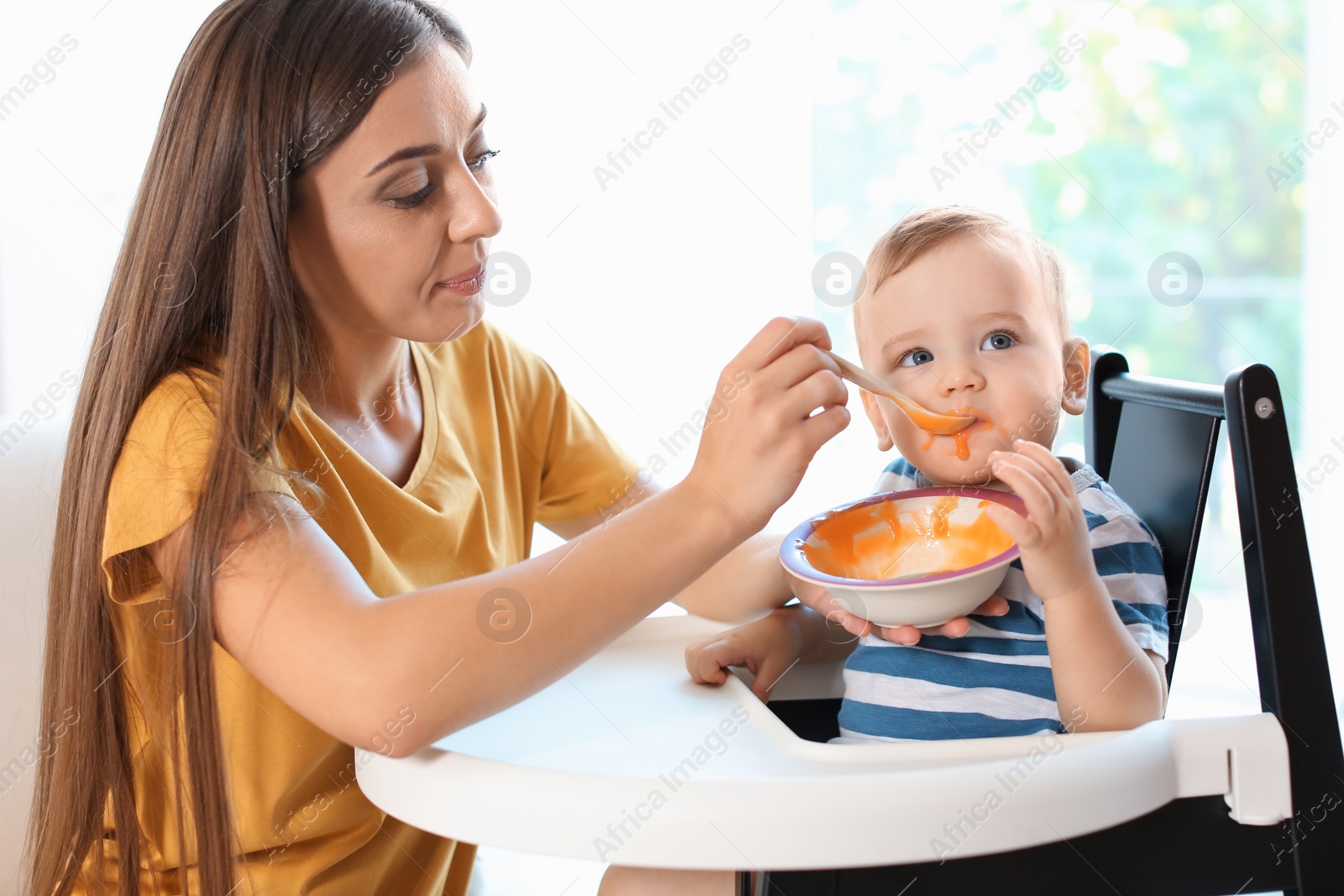 Photo of Woman feeding her child in highchair indoors. Healthy baby food