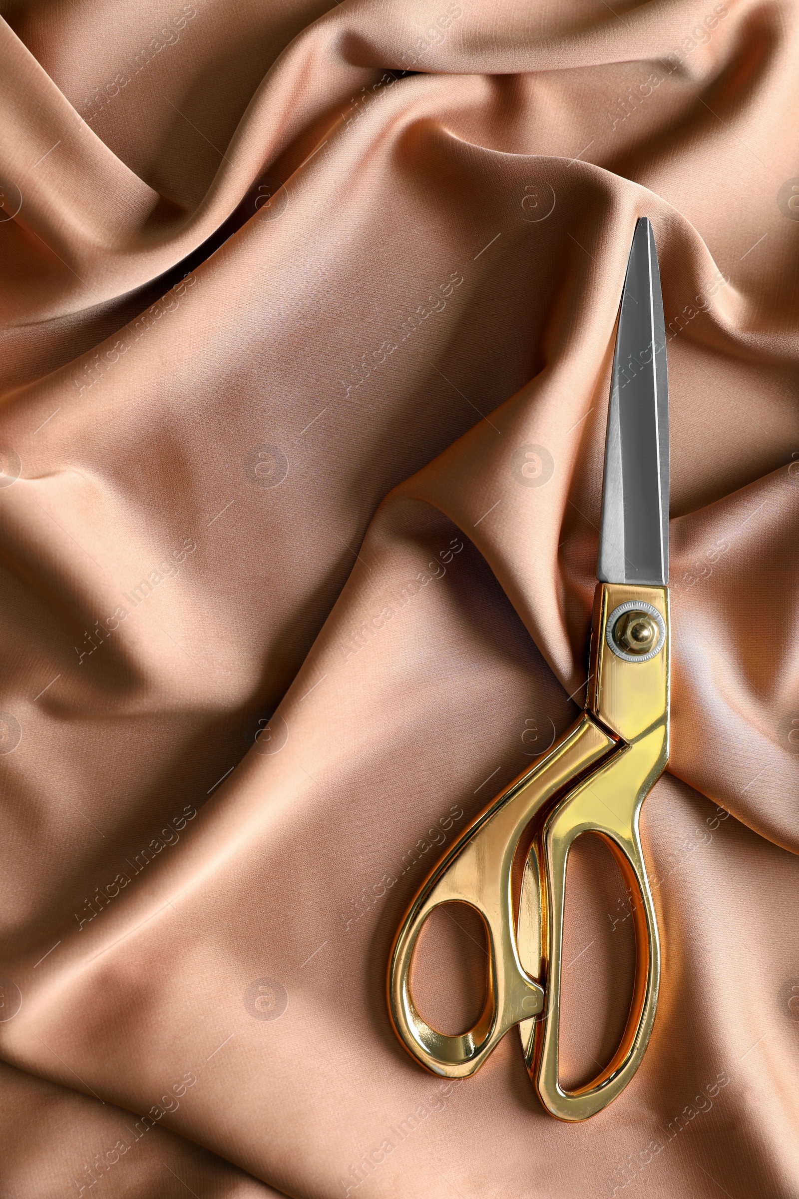 Photo of Scissors for tailoring on silk fabric, top view