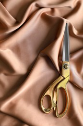 Photo of Scissors for tailoring on silk fabric, top view
