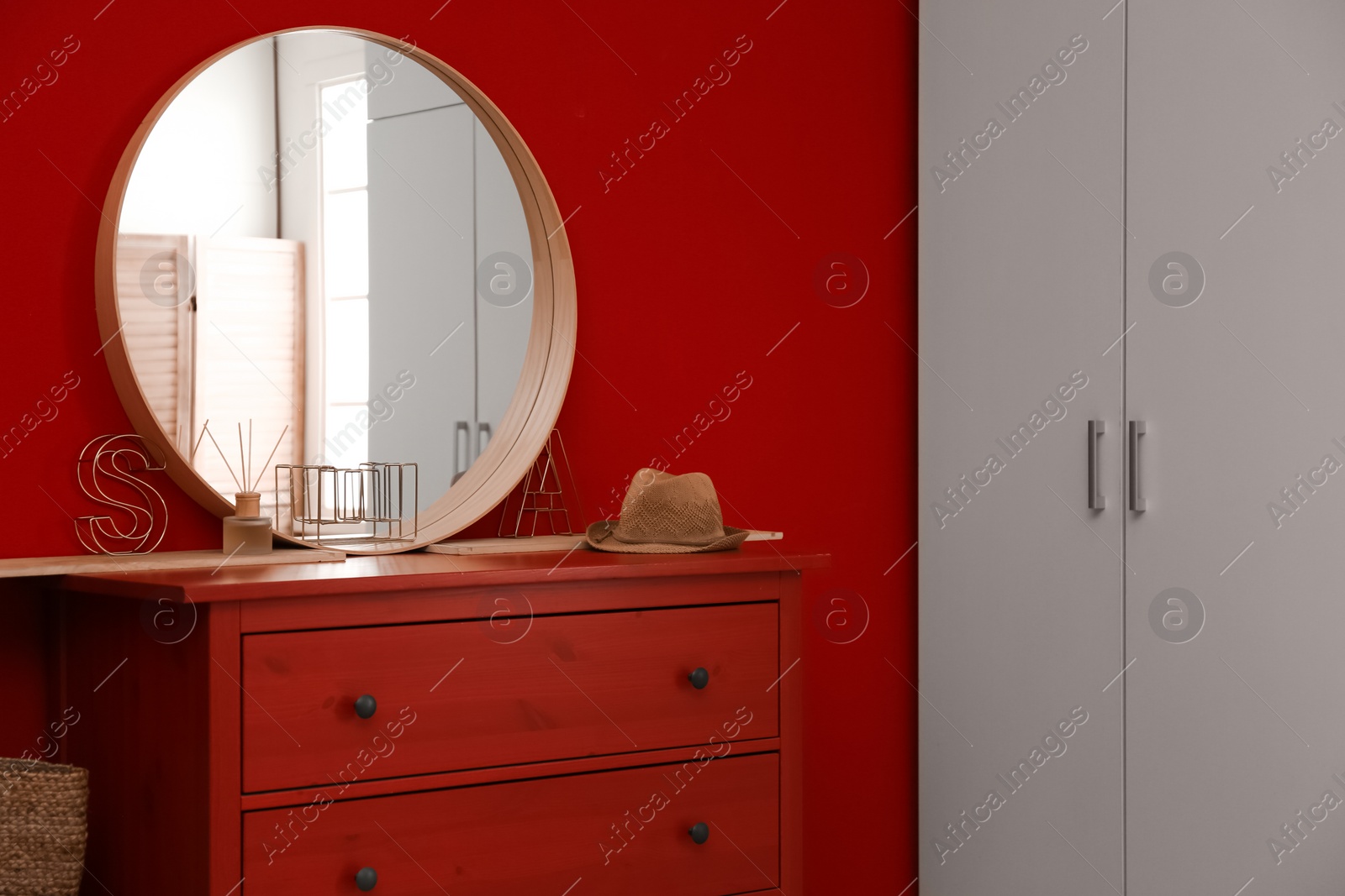 Photo of Round mirror and chest of drawers near red wall in room. Modern interior design