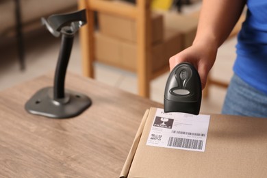 Photo of Post office worker with scanner reading parcel barcode at counter, closeup