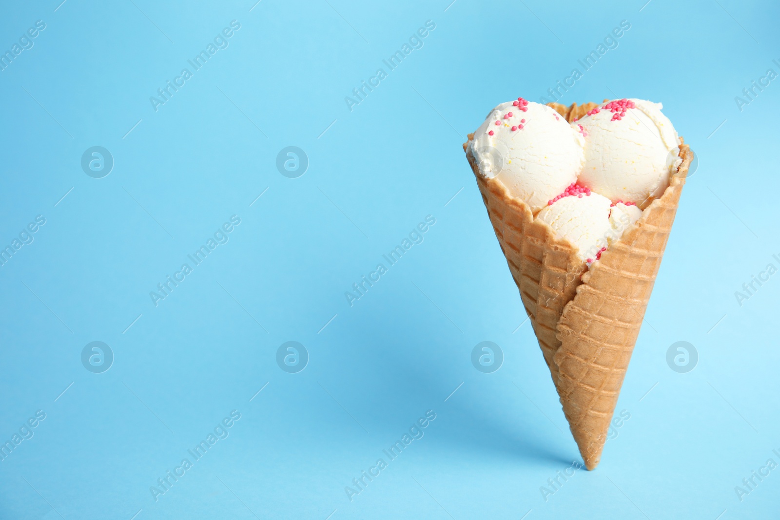 Photo of Delicious vanilla ice cream in wafer cone on blue background. Space for text