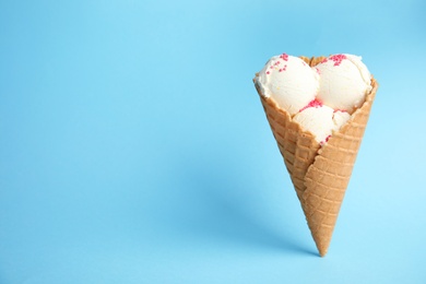 Photo of Delicious vanilla ice cream in wafer cone on blue background. Space for text