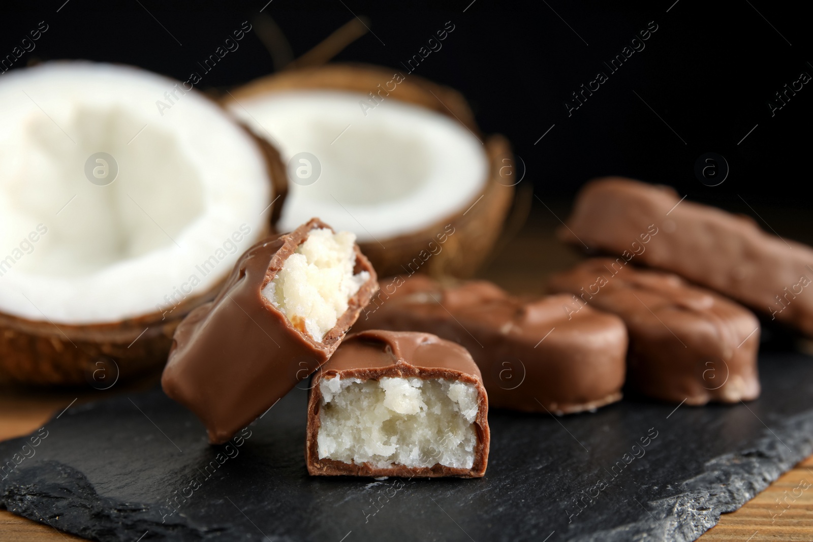 Photo of Delicious milk chocolate candy bars with coconut filling on slate plate, closeup