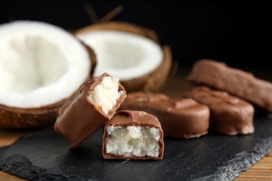 Photo of Delicious milk chocolate candy bars with coconut filling on slate plate, closeup