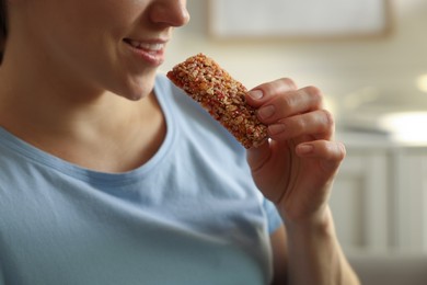 Woman eating tasty granola bar at home, closeup