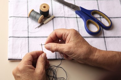 Closeup view of woman threading needle at beige table