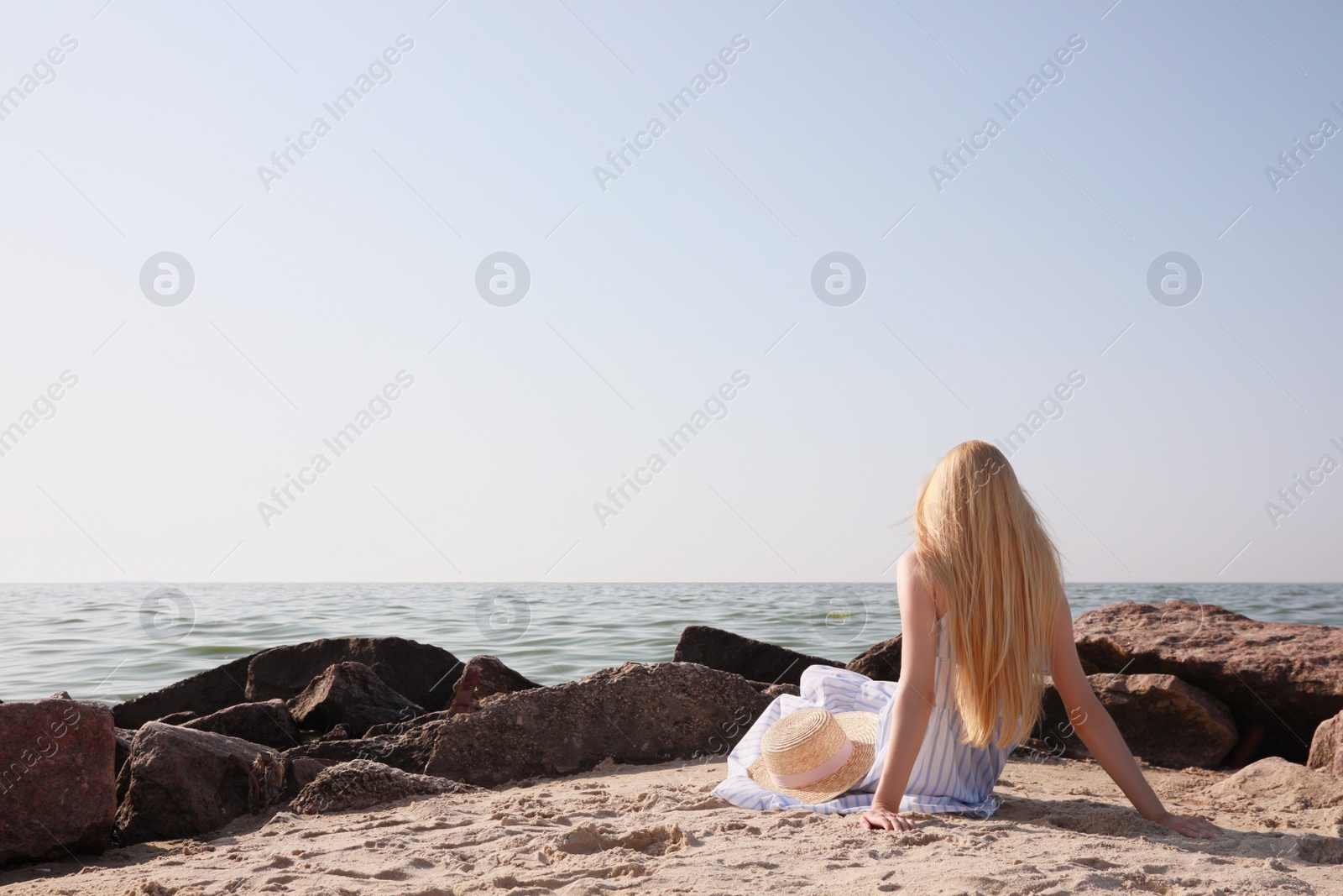 Photo of Young woman with straw hat near sea on sunny day in summer, back view