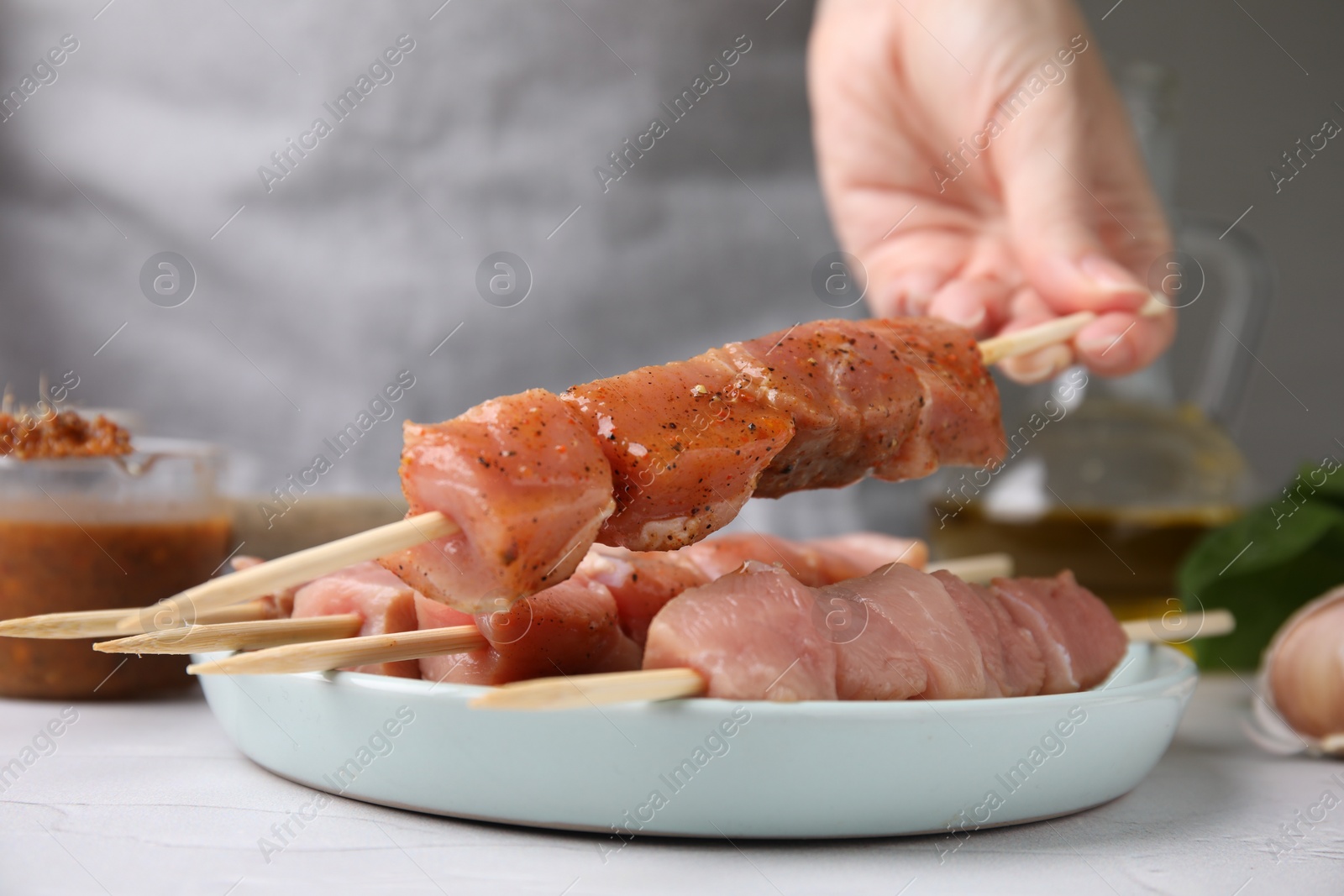 Photo of Woman holding wooden skewer with raw marinated meat at table, closeup