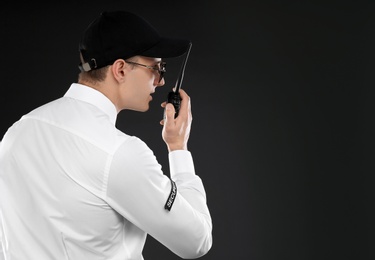 Male security guard using portable radio transmitter on dark background