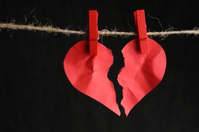 Photo of Halves of torn red paper heart on rope against black background, closeup. Broken heart