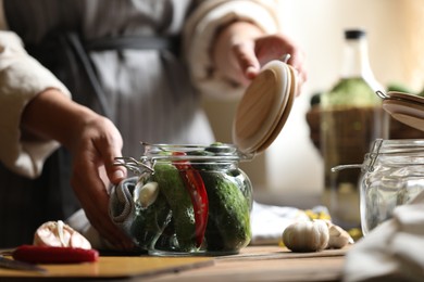 Woman pickling glass jar of cucumbers at wooden table, closeup