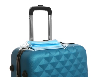 Photo of Stylish blue suitcase and protective masks on white background. Travelling during coronavirus pandemic