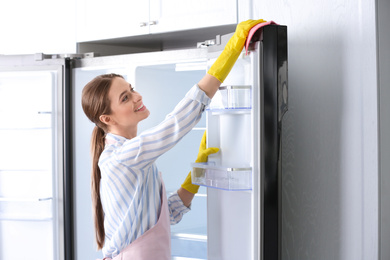 Photo of Woman in rubber gloves cleaning refrigerator at home