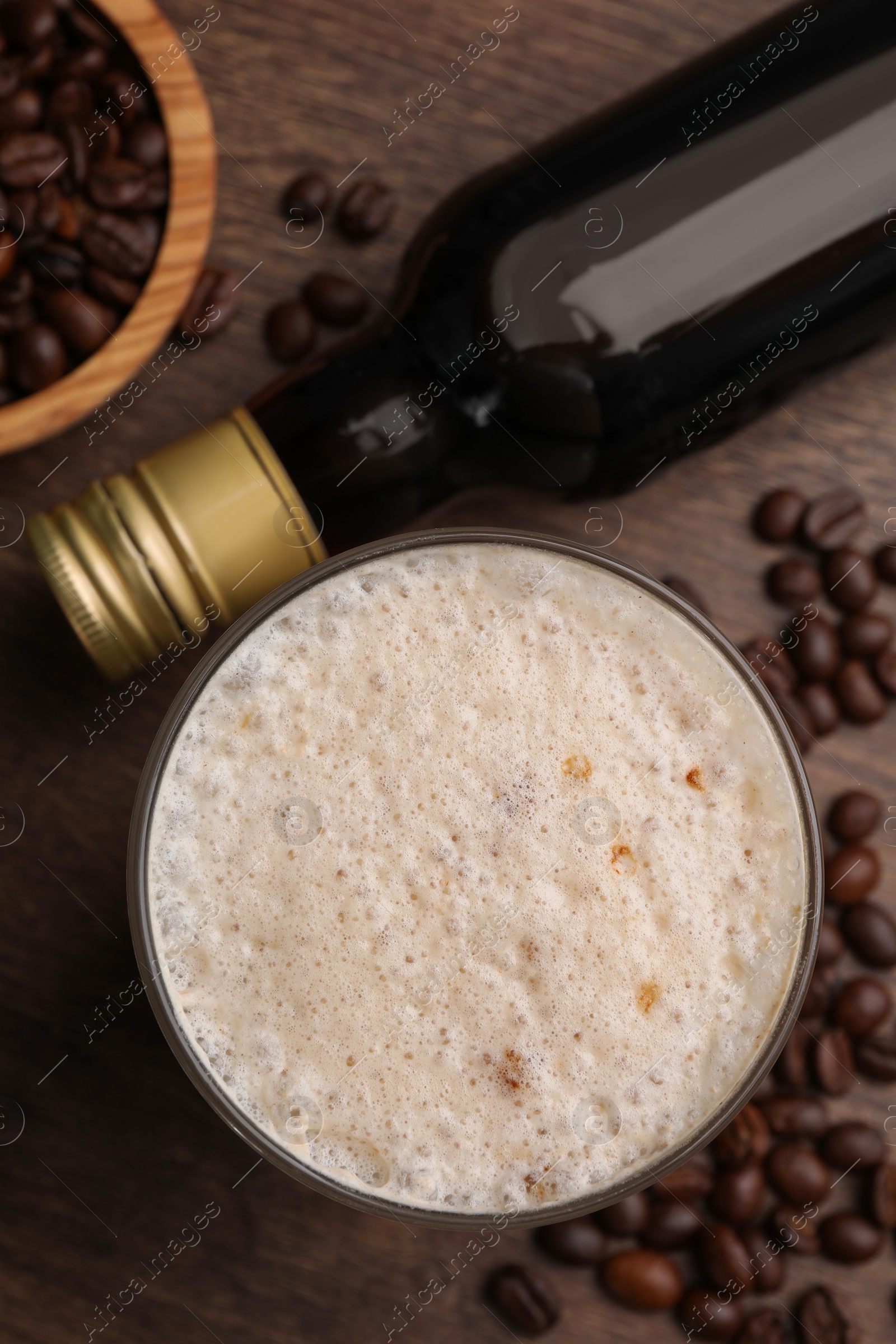 Photo of Bottle of delicious syrup, glass of coffee and beans on wooden table, flat lay