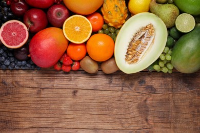 Many different fresh fruits and berries on wooden table, flat lay. Space for text