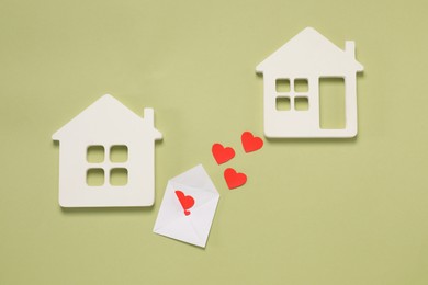 Photo of Long-distance relationship concept. Envelope with paper hearts between two white house models on green background, flat lay