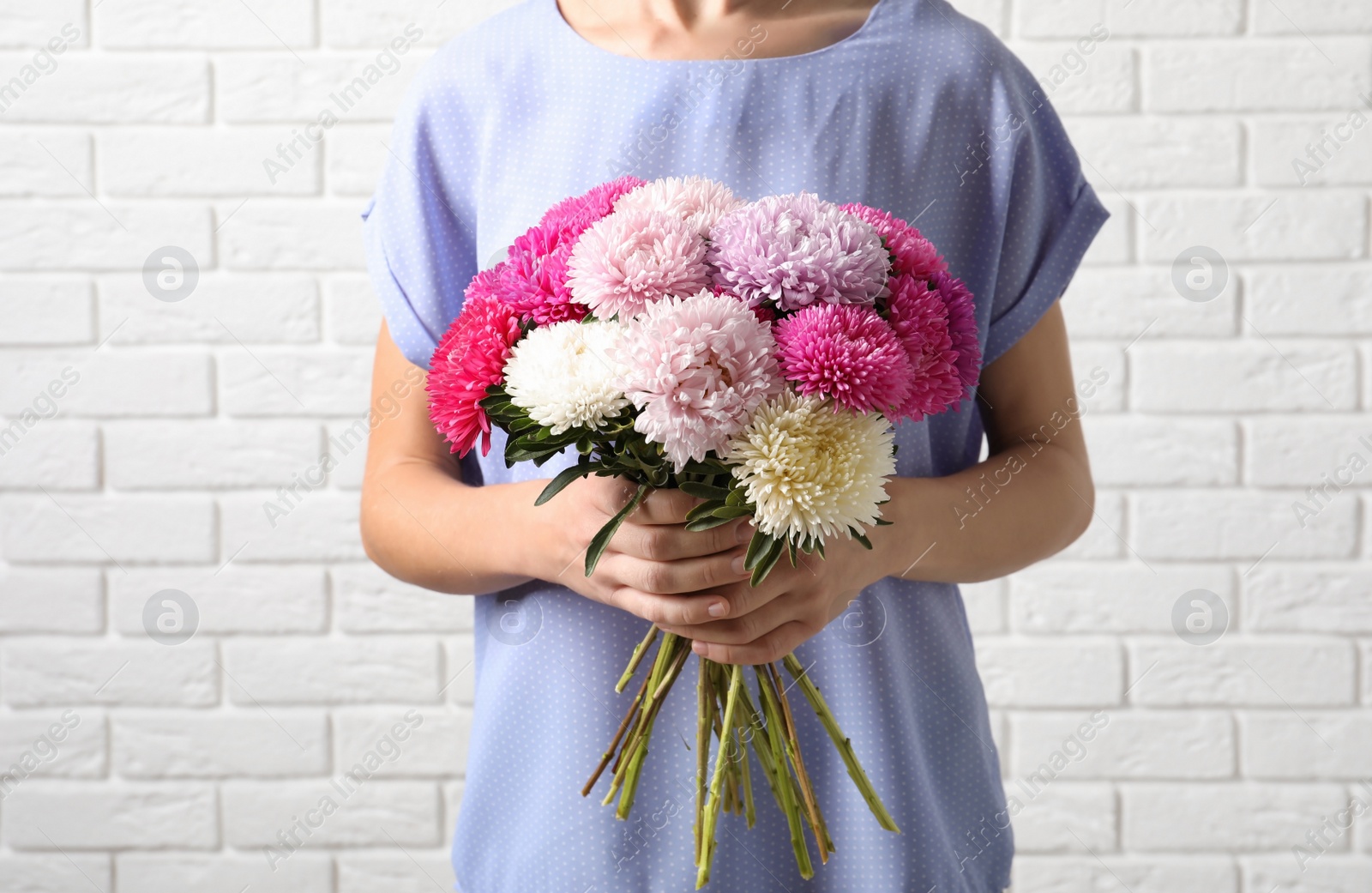 Photo of Woman holding beautiful aster flower bouquet against brick wall