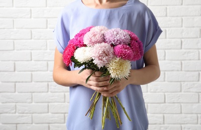 Woman holding beautiful aster flower bouquet against brick wall