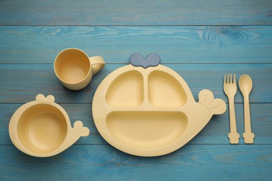 Set of plastic dishware on light blue wooden background, flat lay. Serving baby food