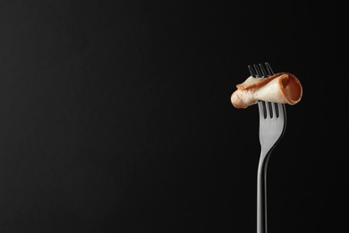 Photo of Fork with slice of ham on black background, space for text