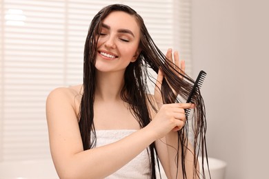 Young woman brushing hair after applying mask in bathroom