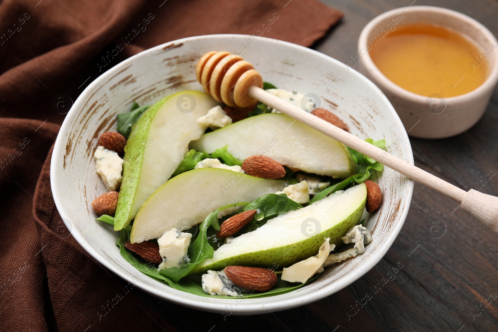 Photo of Delicious pear salad in bowl, honey and dipper on wooden table, closeup