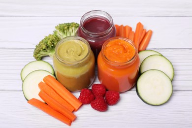 Photo of Jars with healthy baby food and ingredients on white wooden table