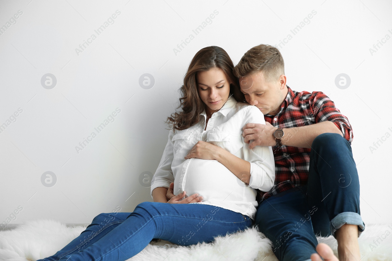 Photo of Pregnant woman with her husband near white wall. Space for text