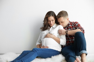 Pregnant woman with her husband near white wall. Space for text