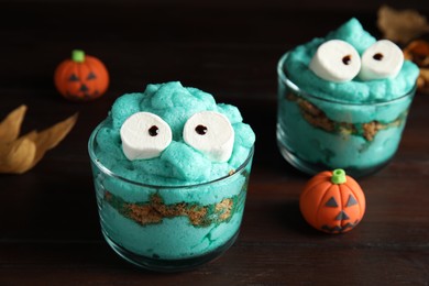 Photo of Delicious desserts decorated as monsters on wooden table, closeup. Halloween treat