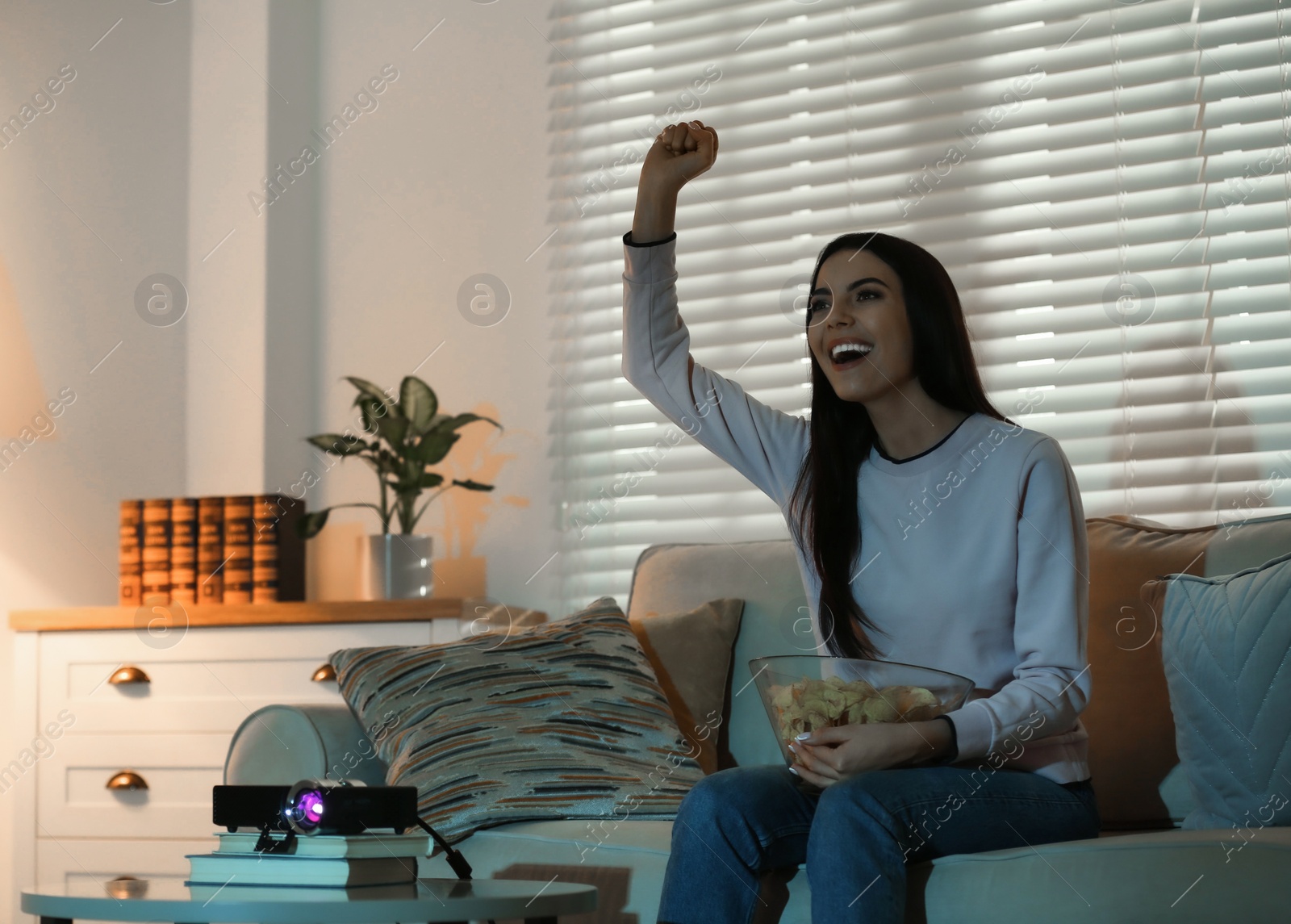 Photo of Emotional young woman watching TV using video projector at home