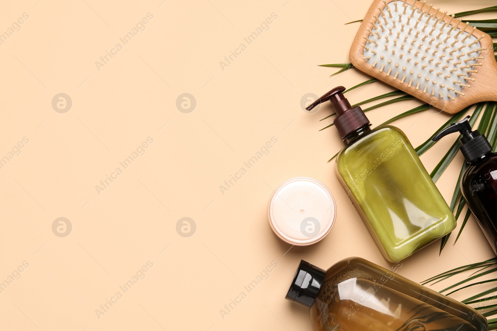 Photo of Shampoo bottles, hair mask, hair brush and palm leaf on beige background, flat lay. Space for text