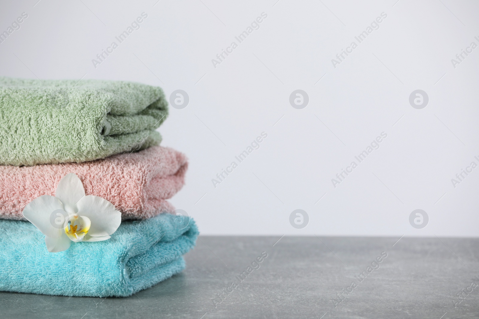 Photo of Stacked soft colorful towels with flower on grey table, space for text