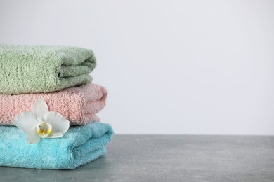 Photo of Stacked soft colorful towels with flower on grey table, space for text