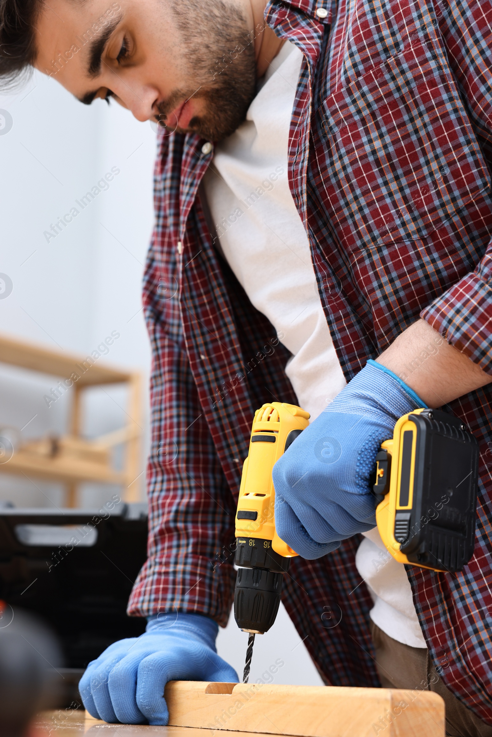 Photo of Young handyman working with electric drill at table in workshop, closeup