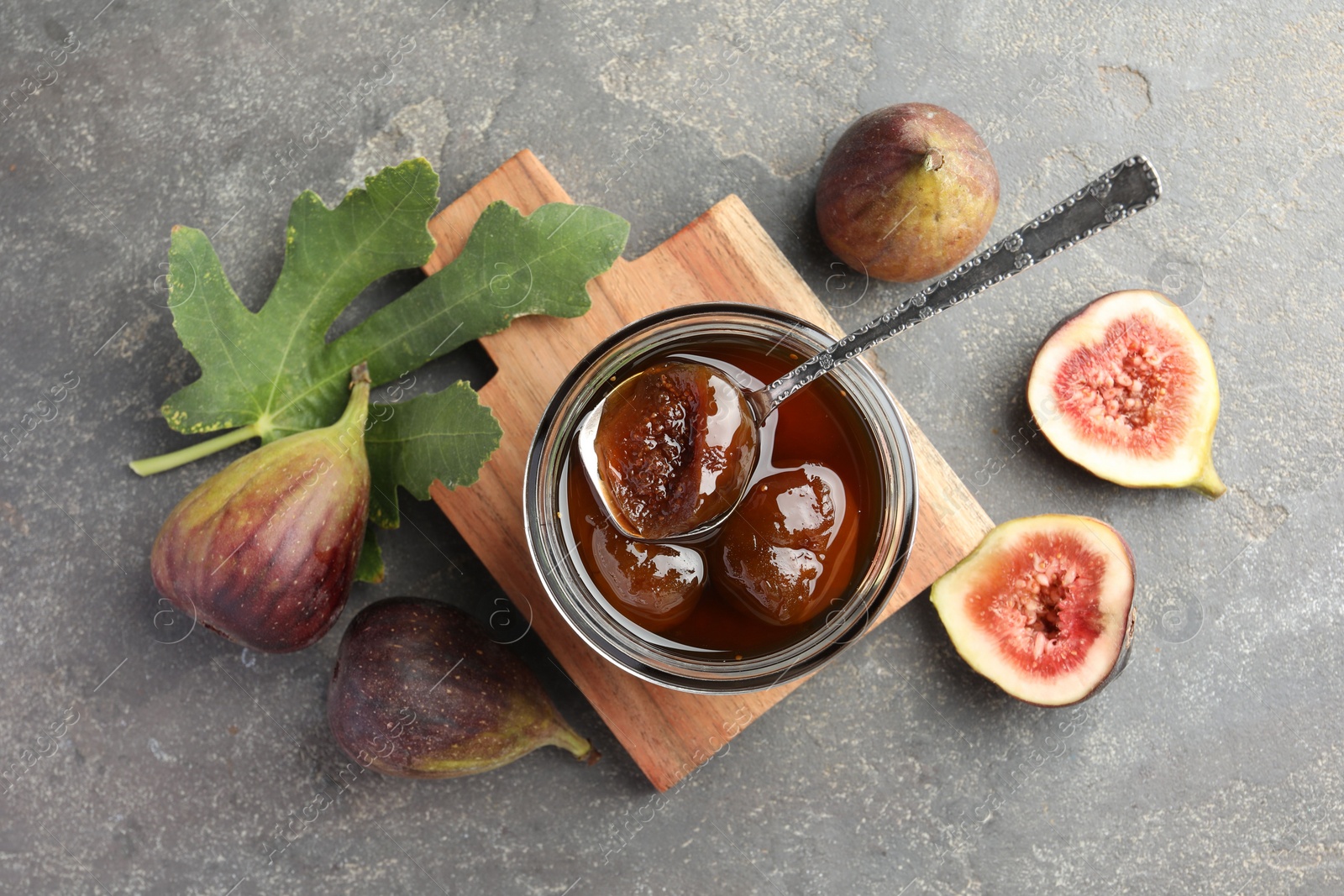 Photo of Jar of tasty sweet jam, fresh figs and green leaf on grey table, flat lay