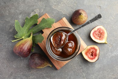 Photo of Jar of tasty sweet jam, fresh figs and green leaf on grey table, flat lay