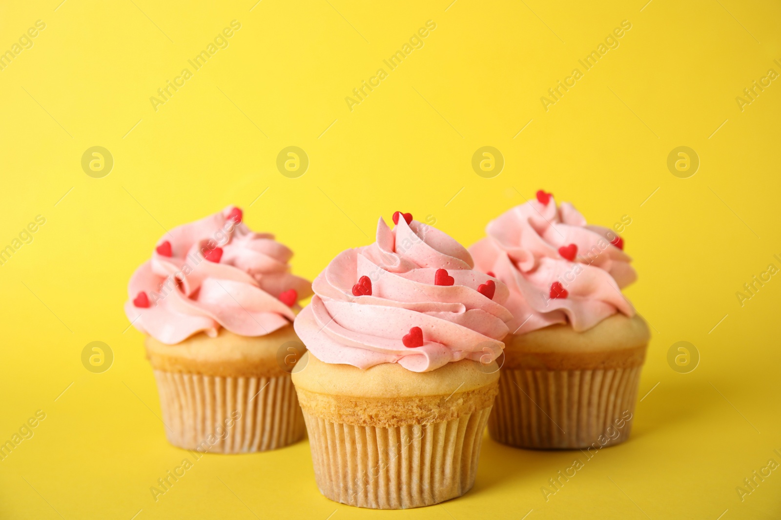 Photo of Tasty cupcakes with heart shaped sprinkles on yellow background. Valentine's Day celebration