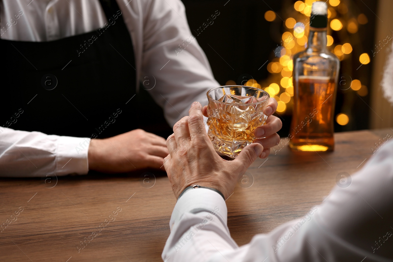 Photo of Bartender giving glass of whiskey to customer at bar counter, closeup